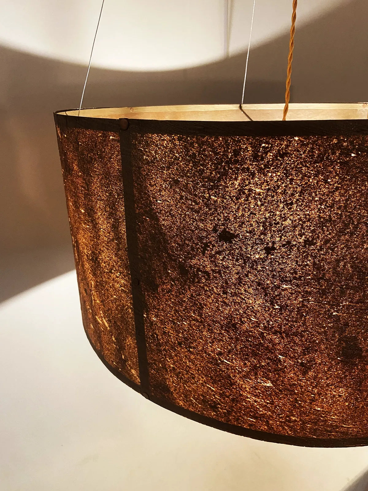 Détail de la suspension en feuille de mica cuivré Thessalie par l'atelier Maus allumée. Rosace et carcasse en acier cuivré, suspendue par 4 cables inox de longueur réglable. Pièce artisanale unique de fabrication française.